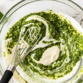 a glass bowl of pesto mayo being mixed.
