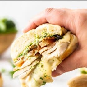 a hand holding a turkey pesto sandwich