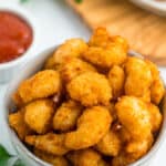 a grey bowl with air fryer popcorn shrimp on a white surface with a small bowl of cocktail sauce.