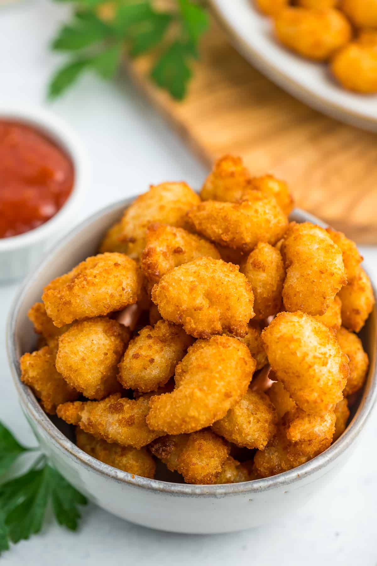 a grey bowl with air fryer popcorn shrimp on a white surface with a small bowl of cocktail sauce.