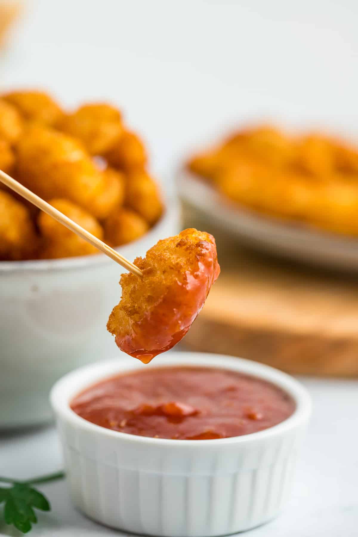a toothpick with a popcorn shrimp hovering over a small white dish of cocktail sauce.