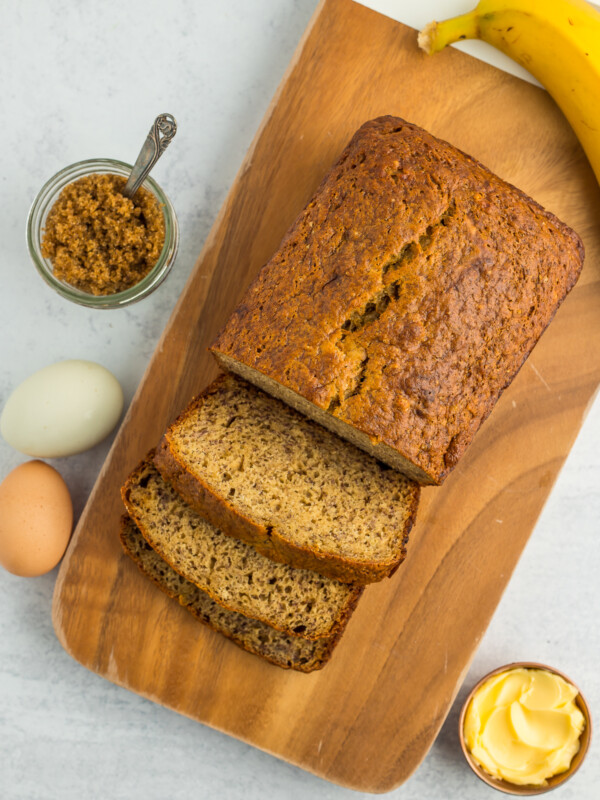 an overhead shot of sliced brown sugar banana bread on a wooden cutting board with a dish of brown sugar.
