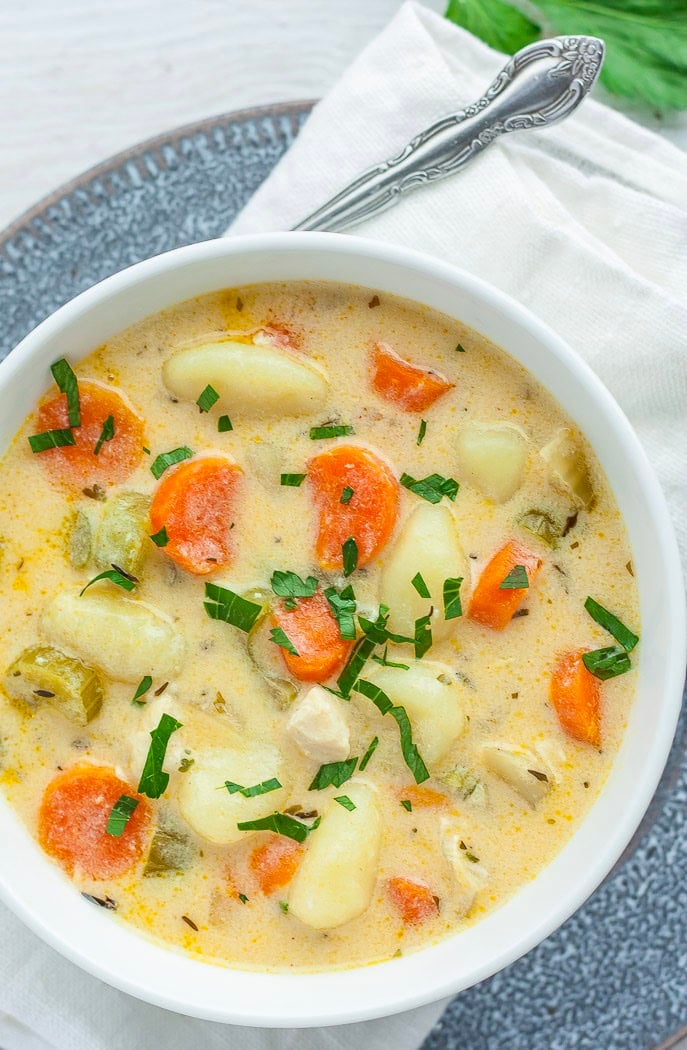 a white bowl of creamy chicken gnocchi soup topped with chopped parsley.