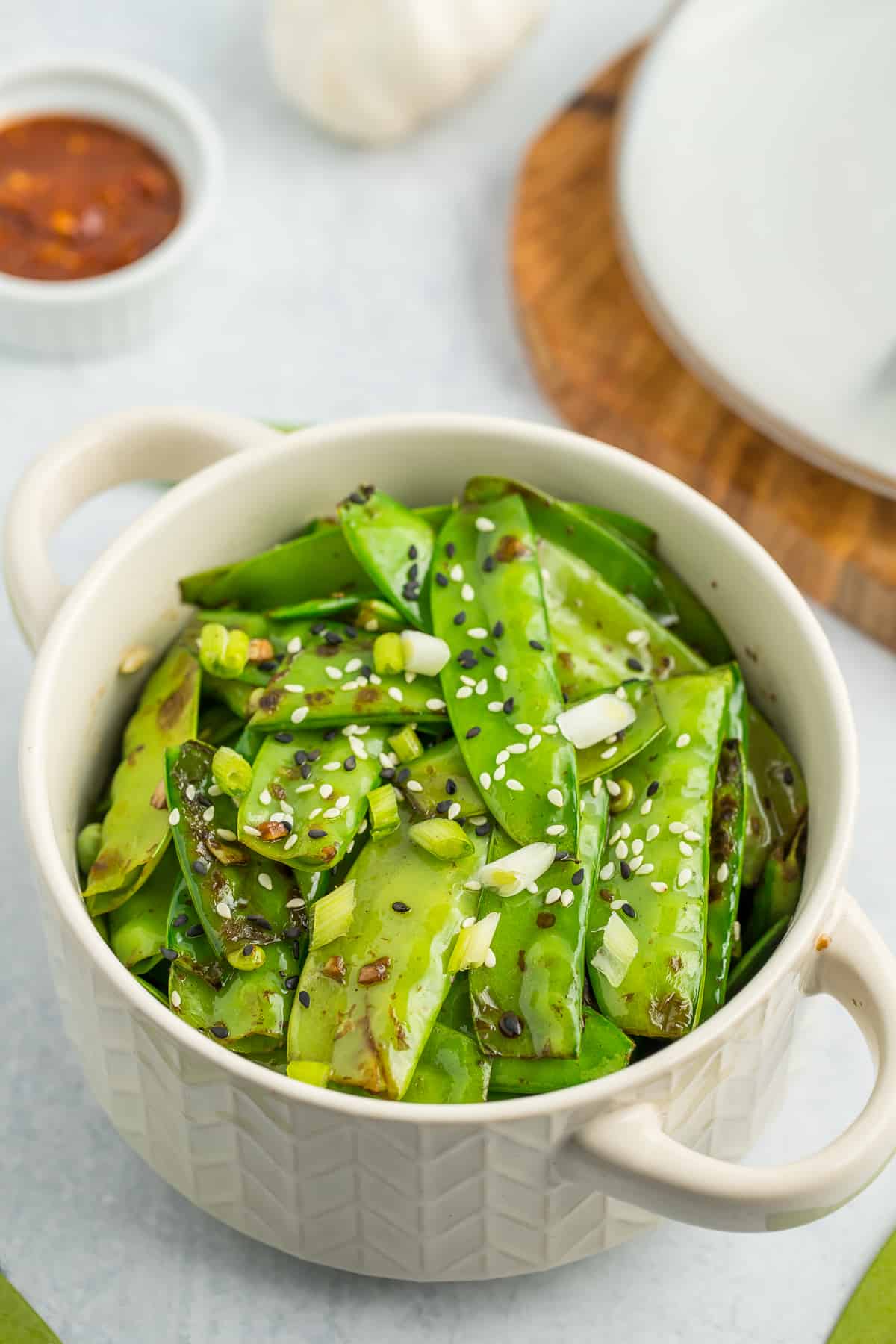 a white bowl with pea pods topped with sesame seeds.