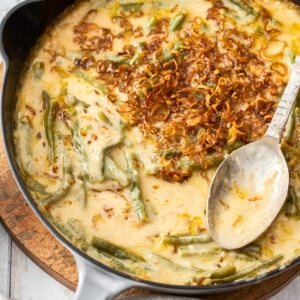 a cast iron skillet with cheesy green bean casserole topped with fried shallots on a wooden board.