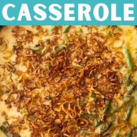 a cast iron skillet with cheesy green bean casserole topped with fried shallots on a wooden board.