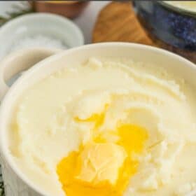 A white textured bowl filled with cream cheese mashed potatoes with melting butter on top.