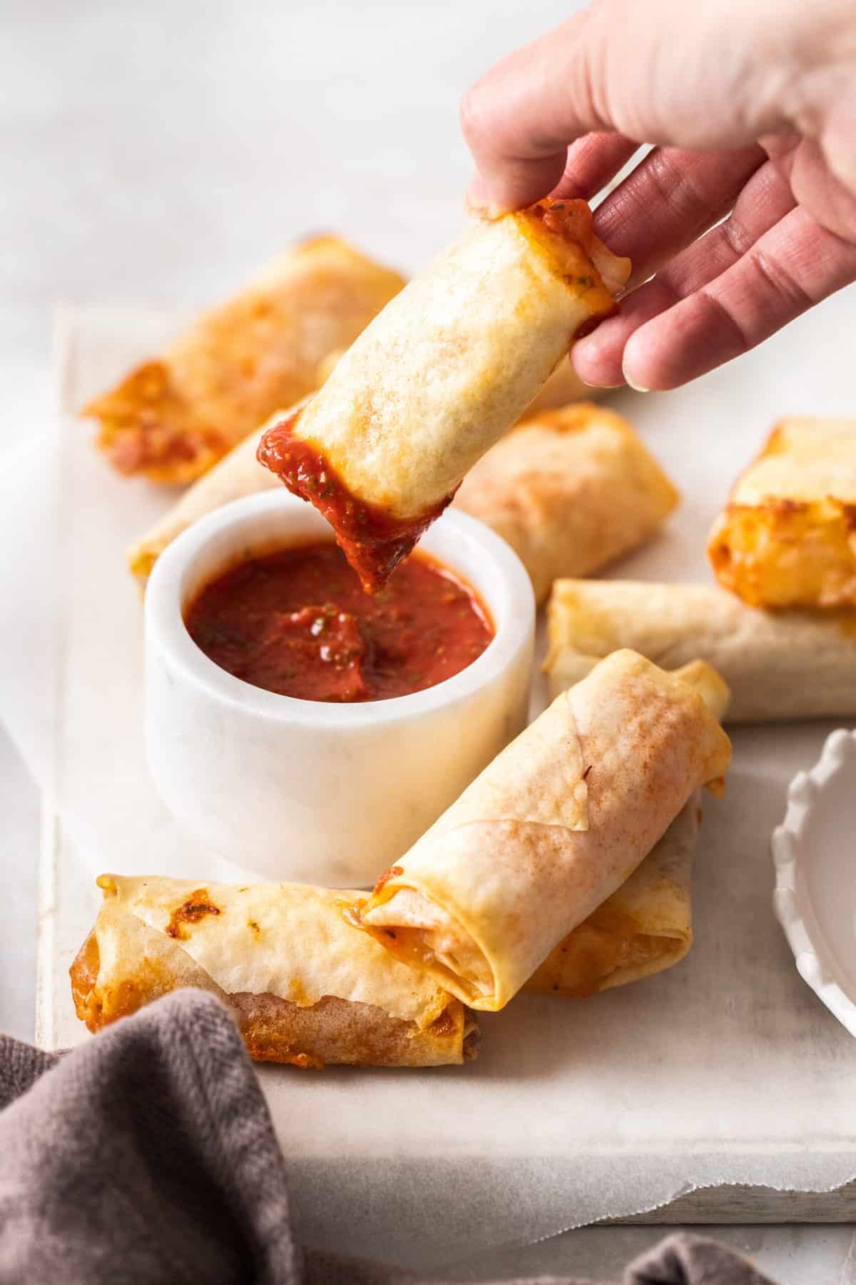 a hand dipping a homemade pizza roll into a bowl of pizza sauce.