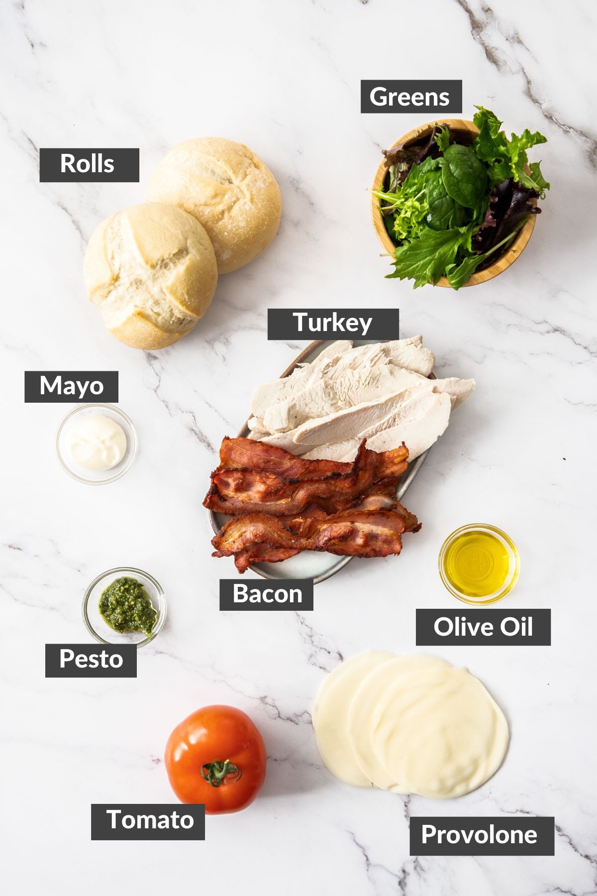bacon, tomato, pesto, cheese, and other ingredients on a marbled board.