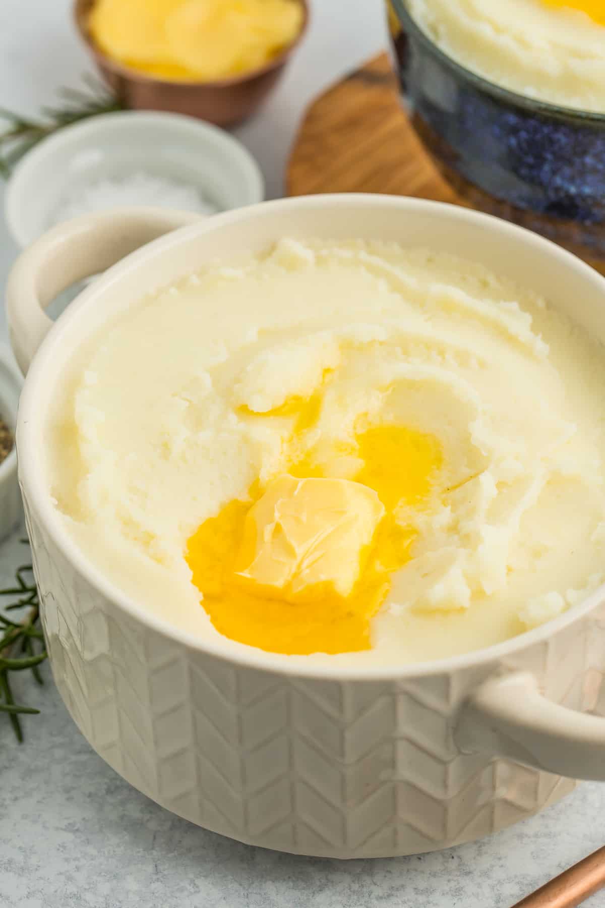 A white textured bowl filled with cream cheese mashed potatoes with melting butter on top.