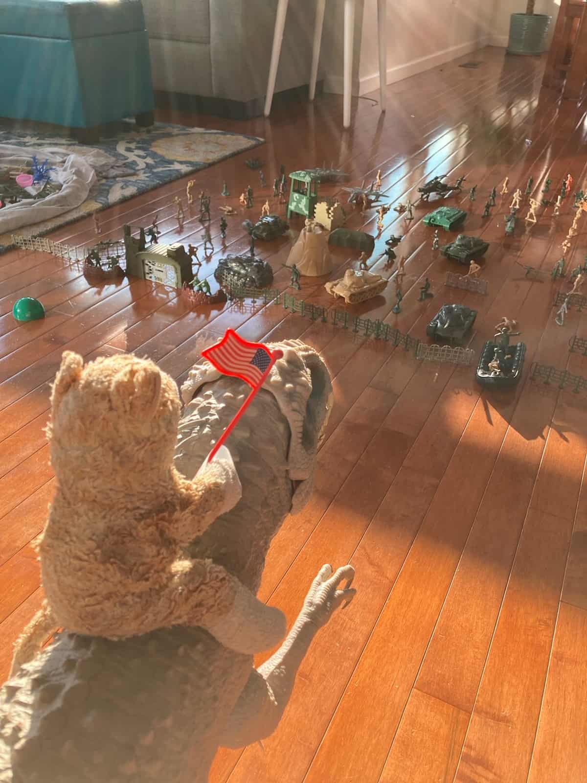 a stuffed cat on a toy dino in front of a line of army soliders.