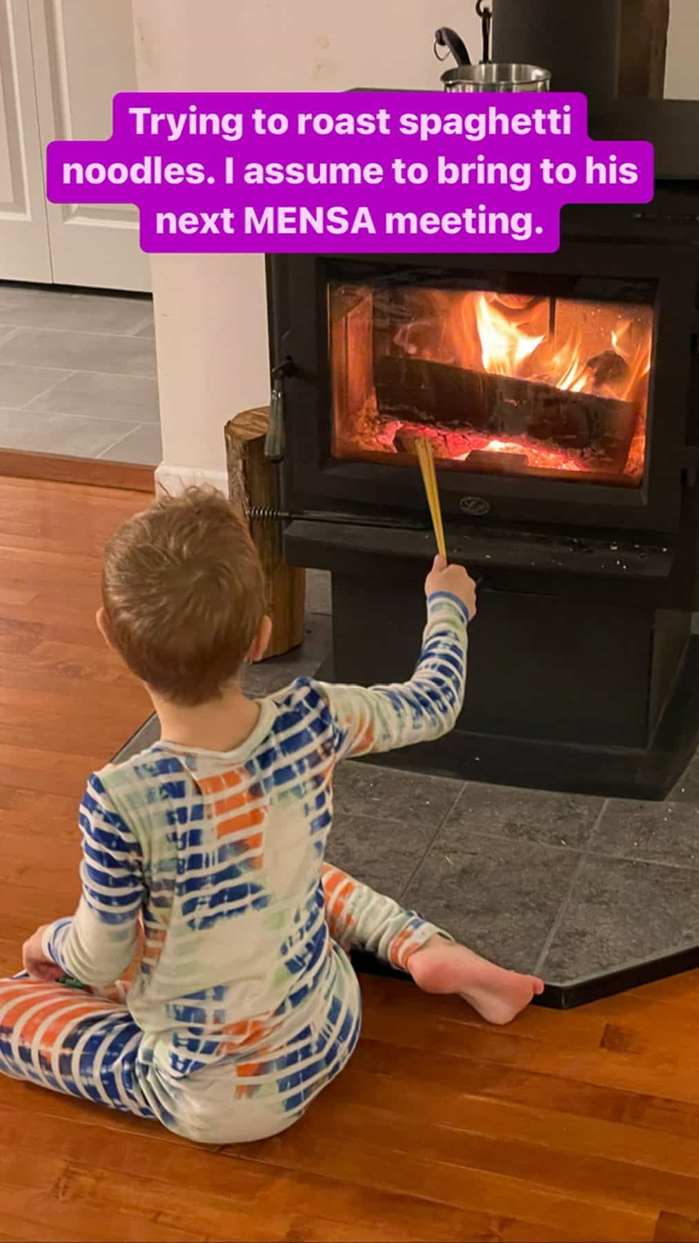 a kid in front of a woodstove holding spaghetti noodles.