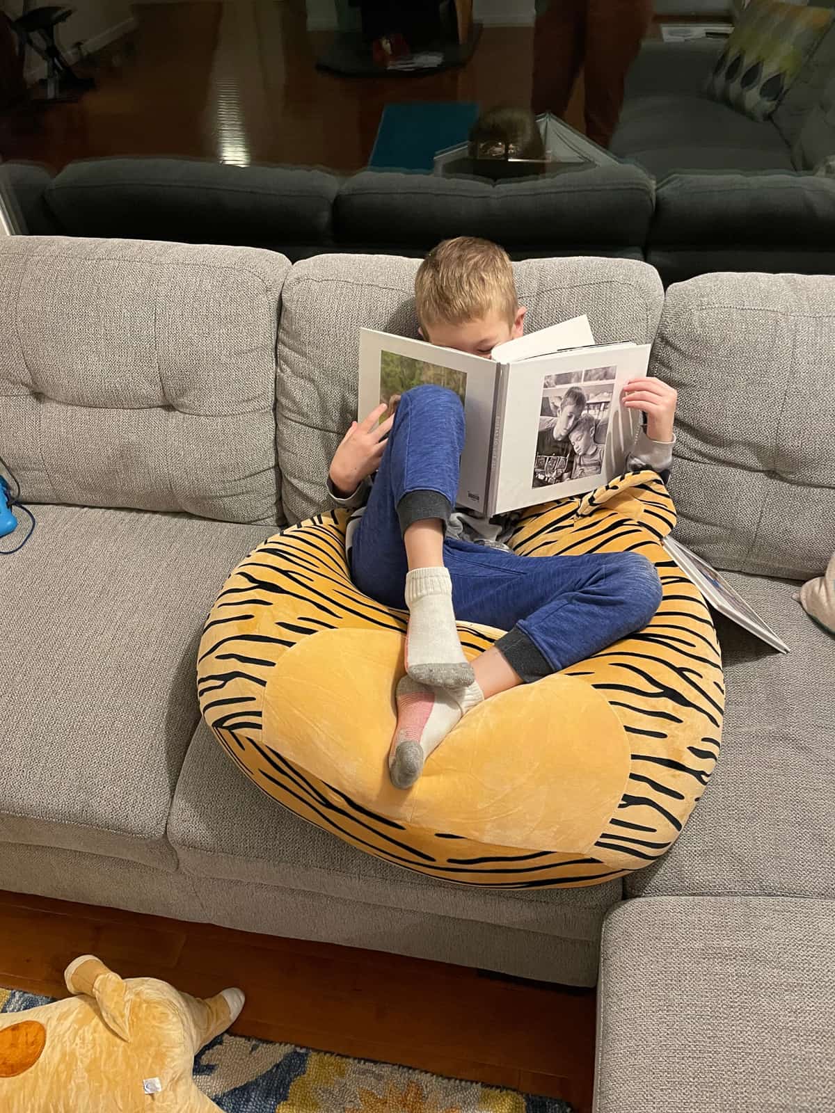 a boy reading a book on a stuffed tiger.