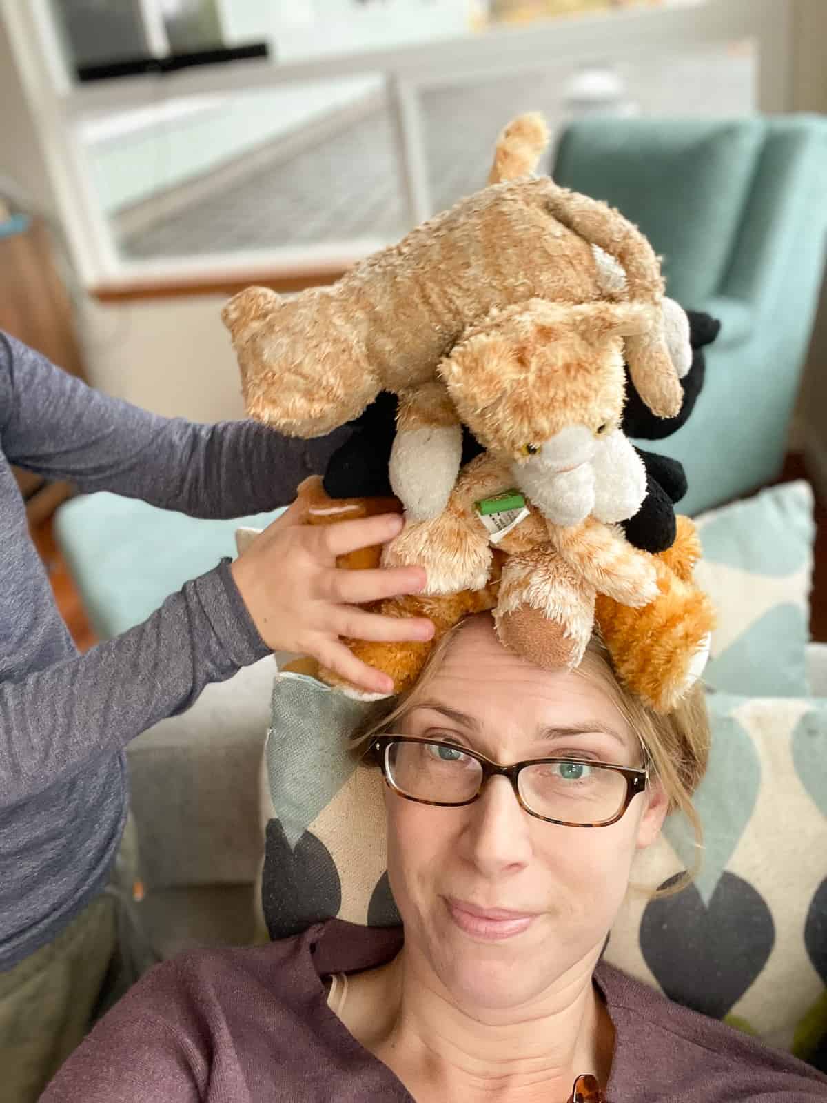  a woman in glasses with stuffed cats stacked on her head.