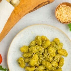 pesto gnocchi on a plate with tomatoes, a fork, and parsley.