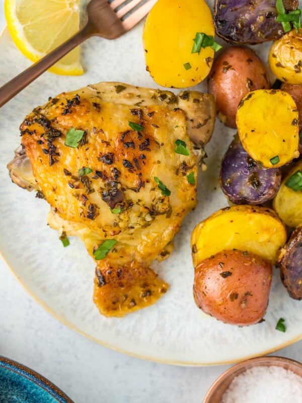 a grey speckled dish with a roasted chicken thigh and potatoes topped with fresh parsley.