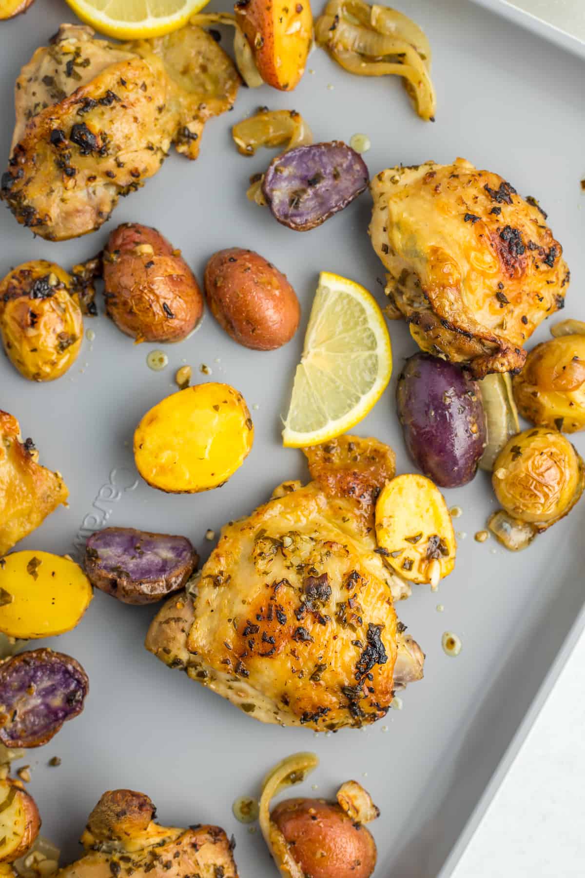 a grey sheet pan with roasted chicken thighs, and sliced potatoes and lemons.