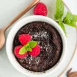 a small lava cake in a white bowl topped with raspberries and mint.