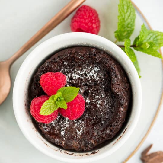 a small lava cake in a white bowl topped with raspberries and mint.