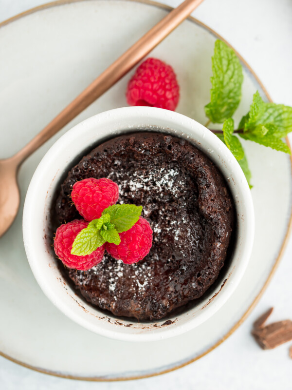 a small lava cake in a white bowl topped with raspberries and mint.