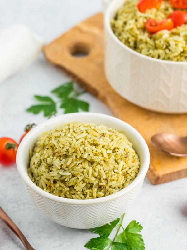 a white bowl of pesto rice with a fork, parsley, and tomatoes.