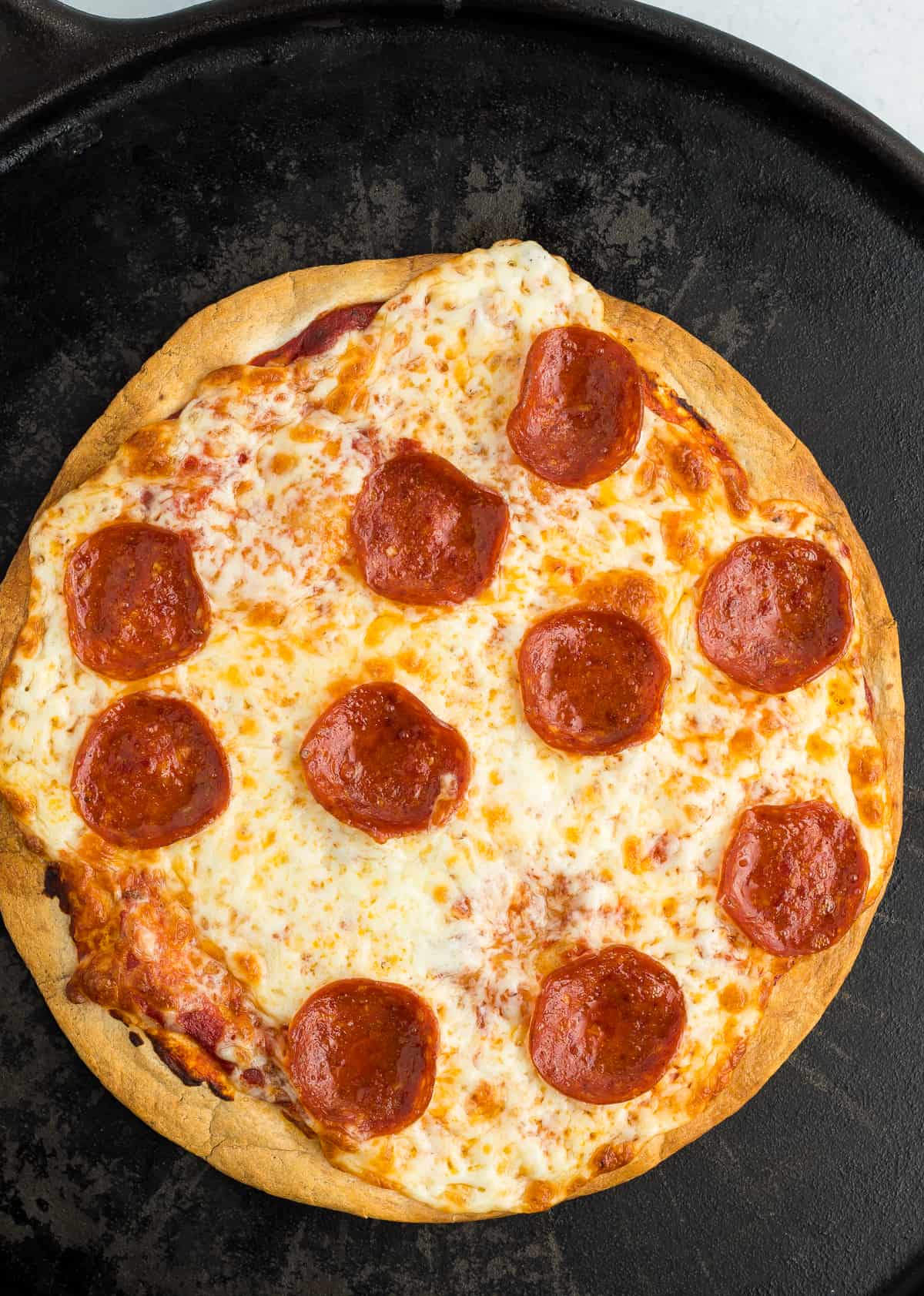 a pizza with pepperonis on a cast iron pizza pan.