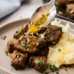 a spoonful of garlic butter being drizzled over air fryer steak bites topped with chopped parsley.