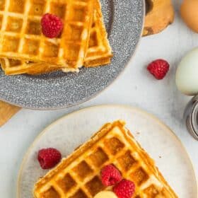 a plate with waffles topped with butter and raspberries.