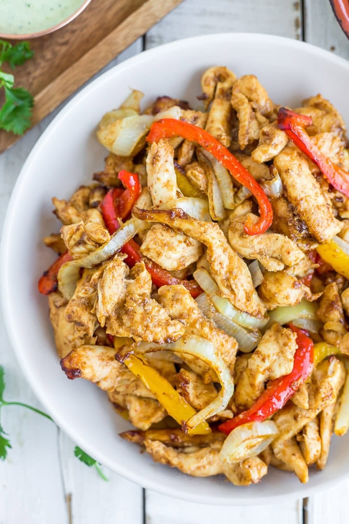 a white bowl of sliced chicken, peppers, and onions.