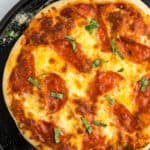 an overhead shot of a pepperoni pizza on a black pizza stone.