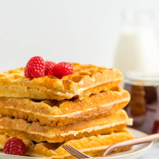 a stack of 4 whole wheat waffles on a plate topped with raspberries.