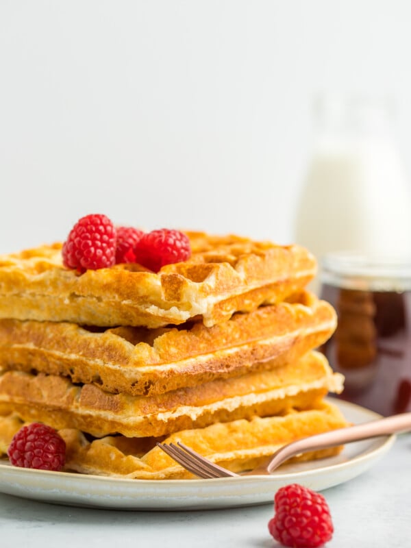 a stack of 4 whole wheat waffles on a plate topped with raspberries.