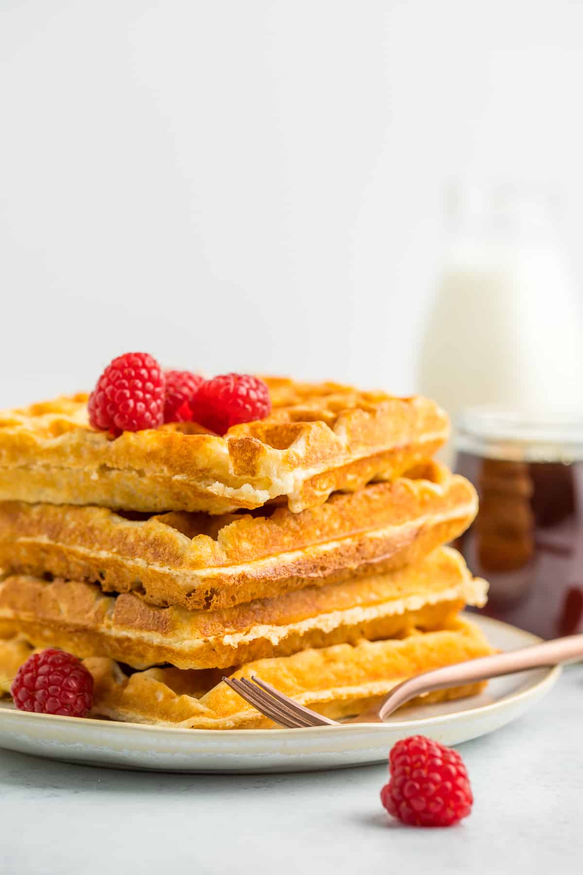 a stack of 4 whole wheat waffles on a plate topped with raspberries.