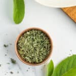 a small metal dish with dried sage in it, and fresh sage leaves on a white board.