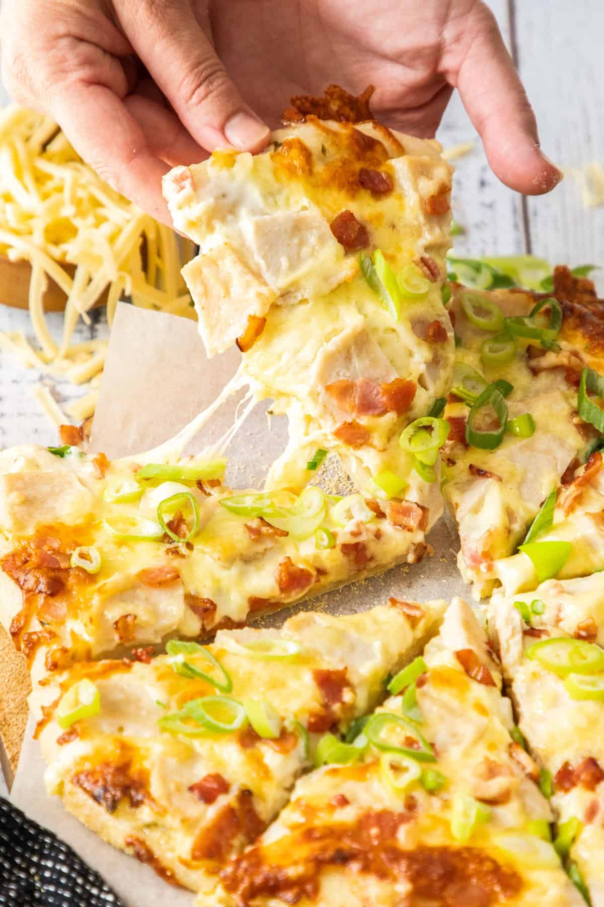 a hand holding a slice of pizza topped with scallions.