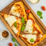 Margherita flatbread topped with basil on a wooden tray.