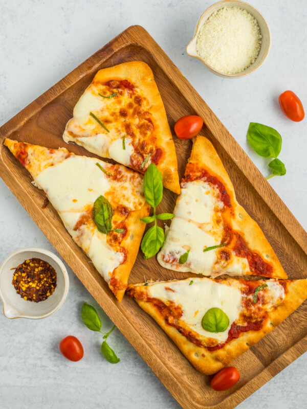 Margherita flatbread topped with basil on a wooden tray.