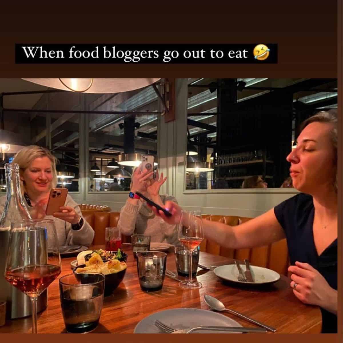 3 women at a restaurant taking photos of food with their phones.