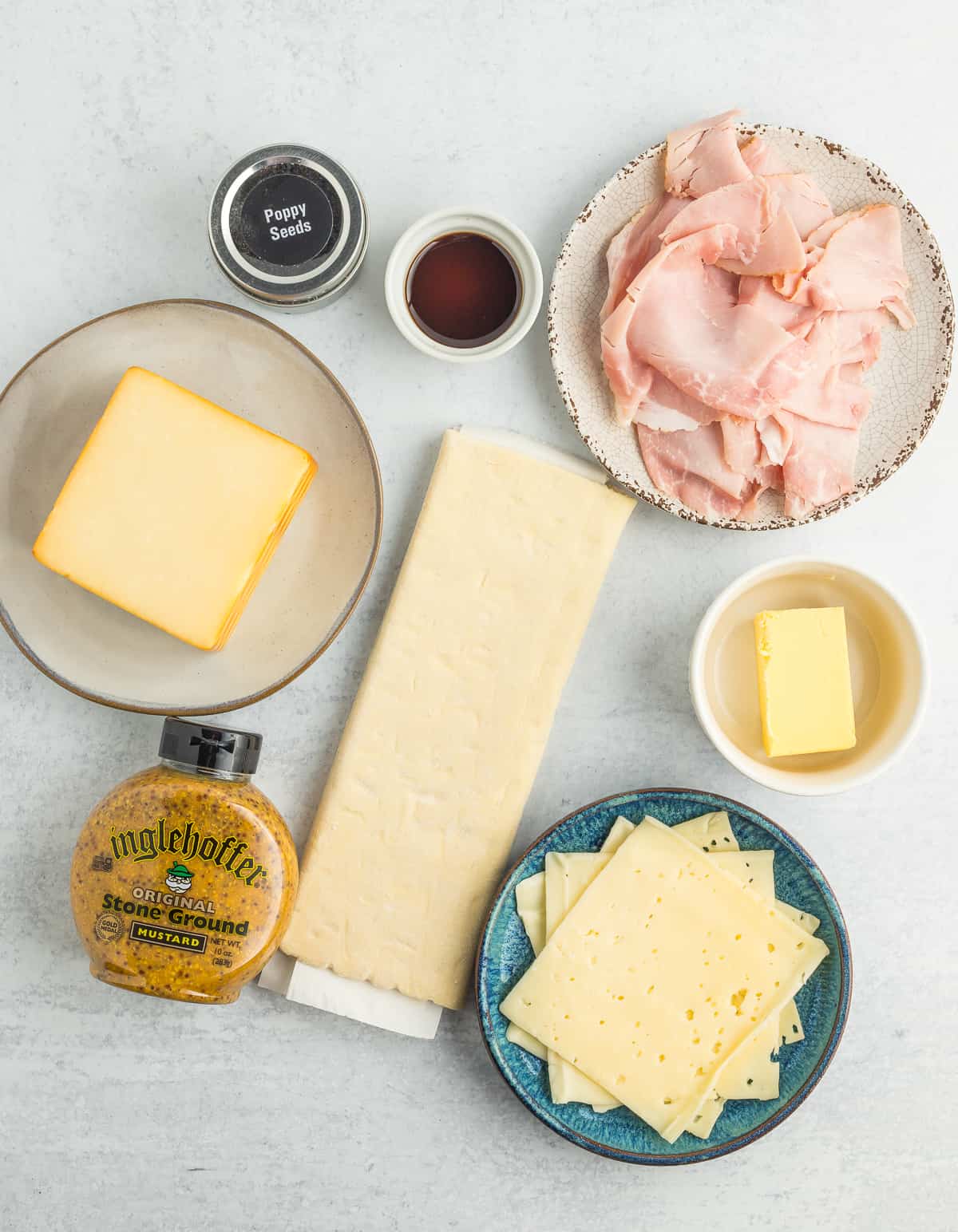 sheets of puff pastry, slices and bowls of cheese and ham and other ingredients on a white board.