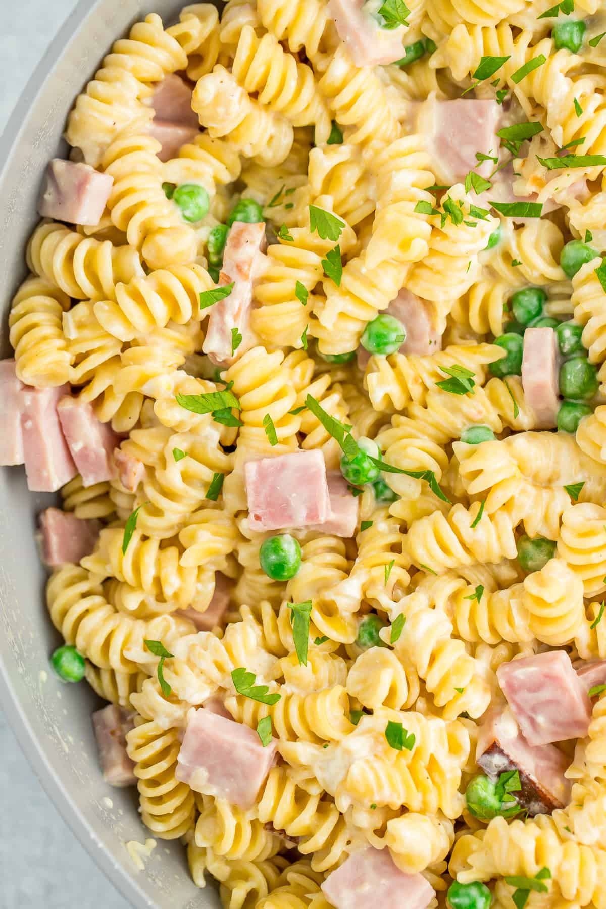 rotini, diced ham, and peas in a skillet topped with fresh chopped parsley.
