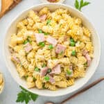 ham and pea pasta in a white bowl with a bronze spoon.