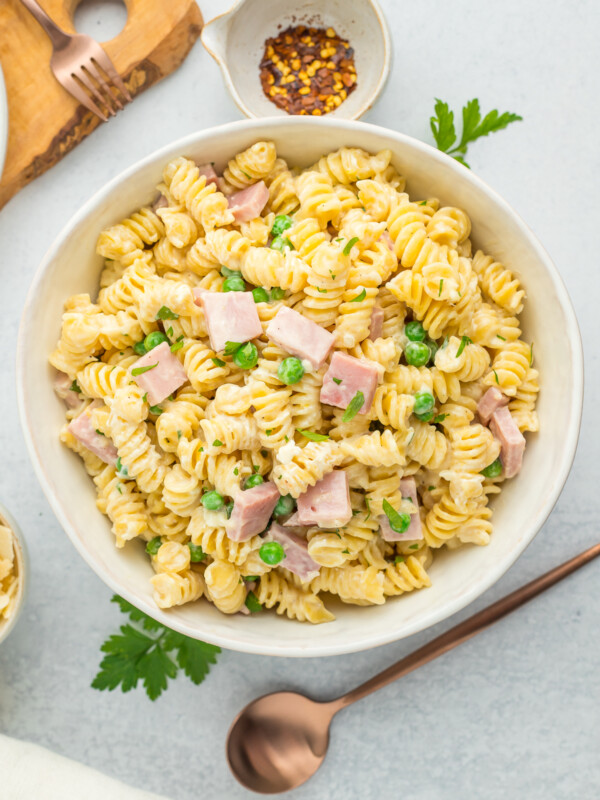 ham and pea pasta in a white bowl with a bronze spoon.