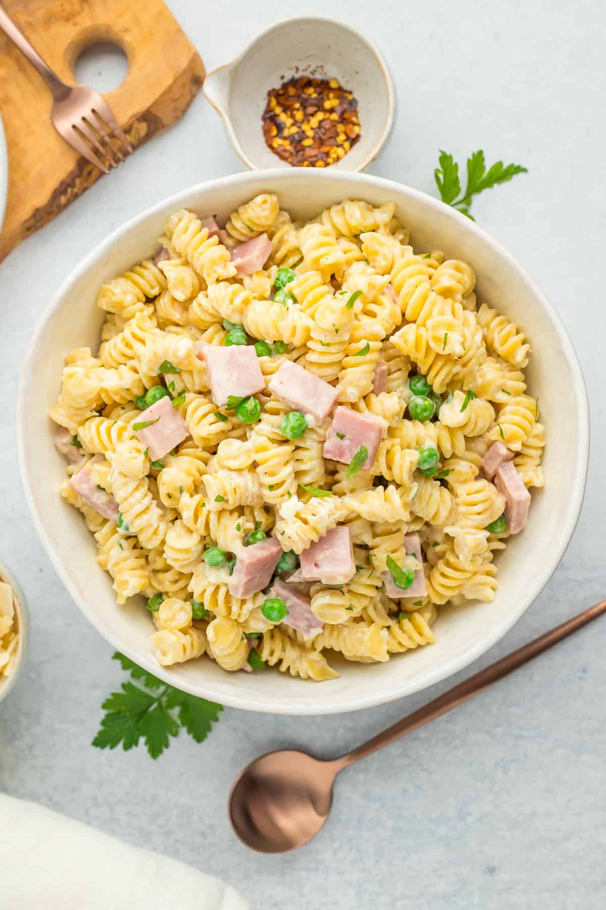 ham and pea pasta in a white bowl with a bronze spoon.