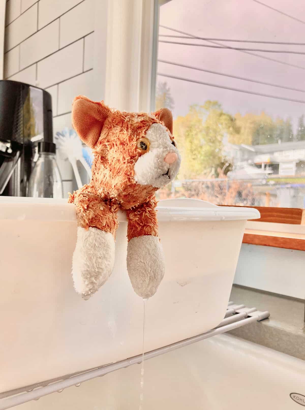 a stuffed cat hanging over the edge of a white tub.