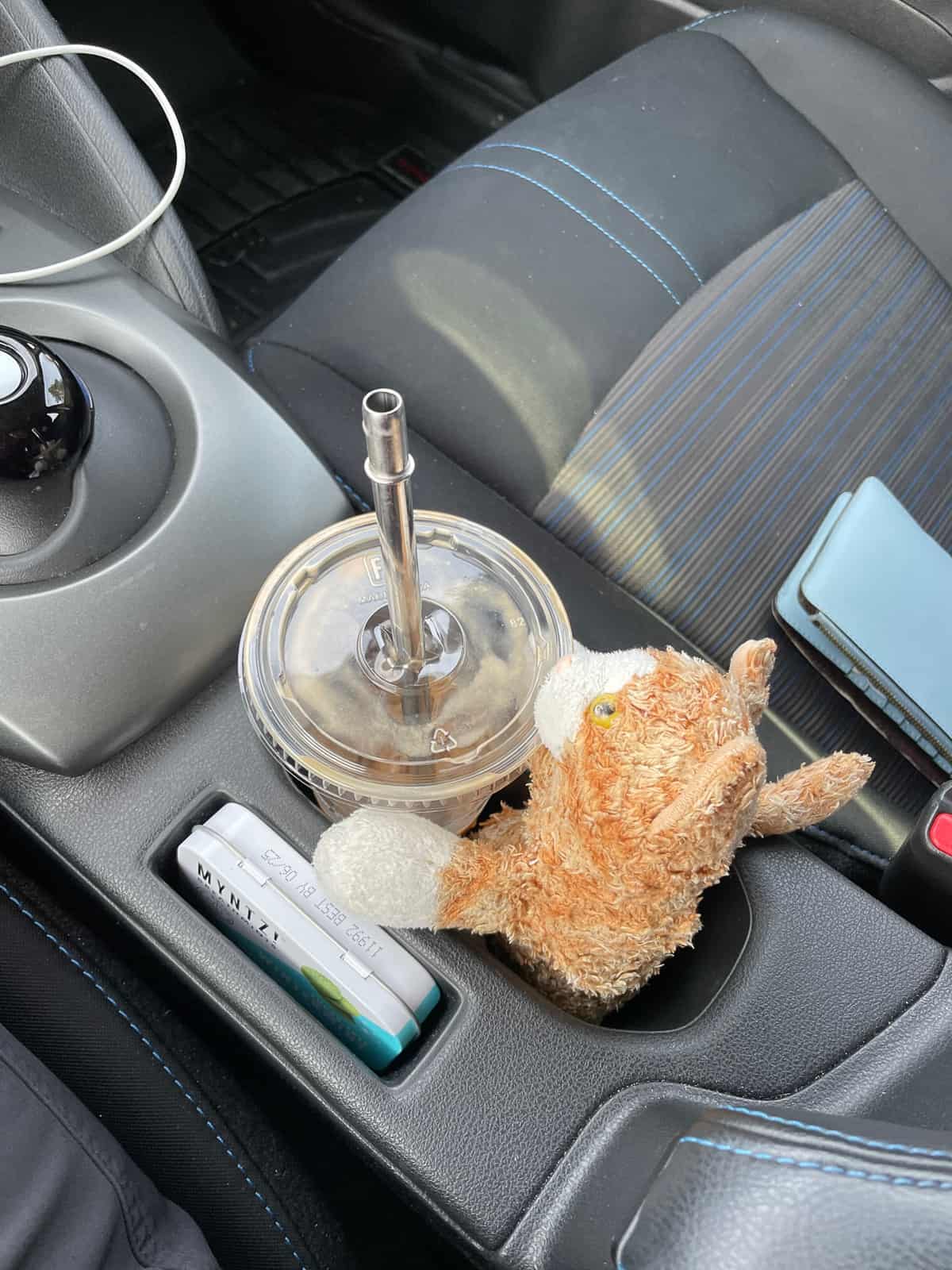 a stuffed cat with a latte in a car's cupholder.