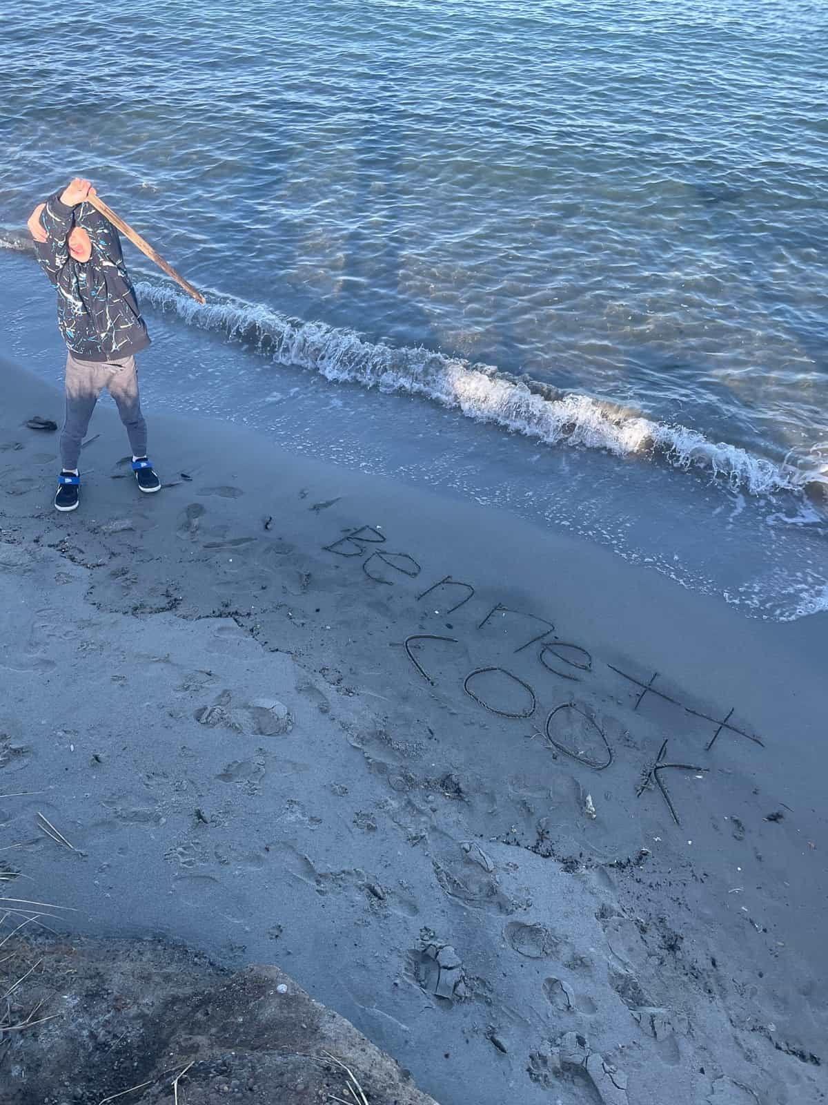 a boy in a beach with writing in the sand.