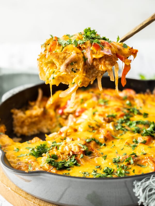 a scoopful of chicken fajita casserole hovering over a cast iron skillet.