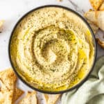 homemade hummus in a black bowl topped with seeds and olive oil.