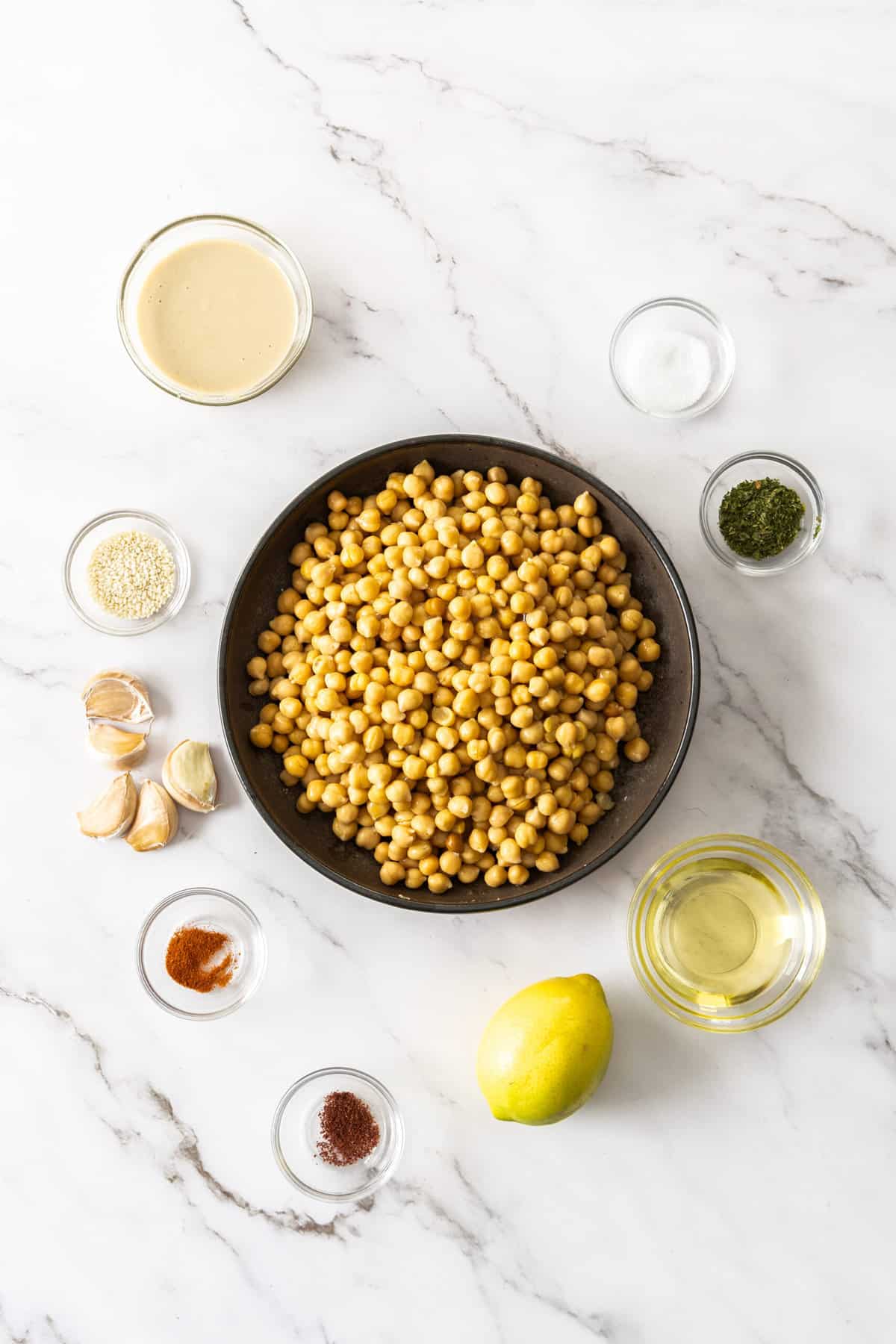 chickpeas, a lemon, garlic, and other ingredients on a marble board.