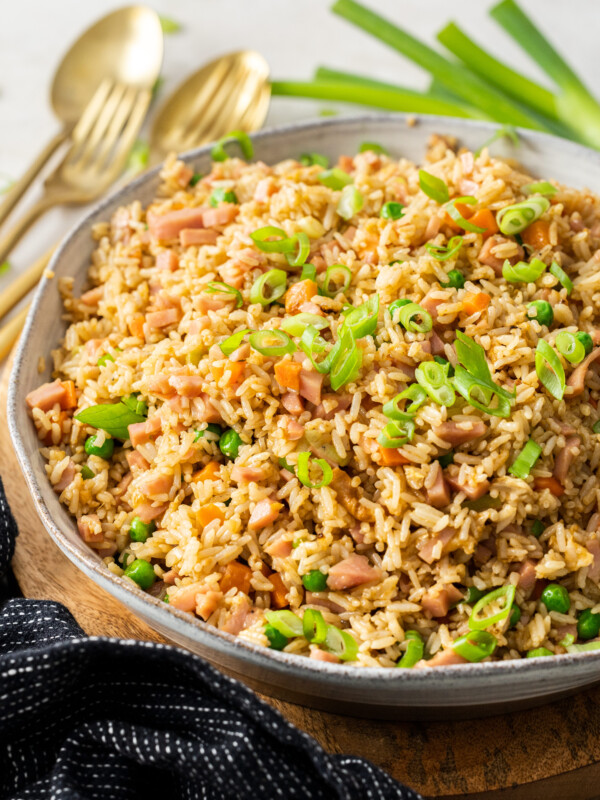 a beige bowl with ham fried rice topped with sliced green onions.
